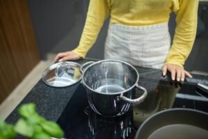 woman in yellow sweater standing by induction cooktop with a steel pot